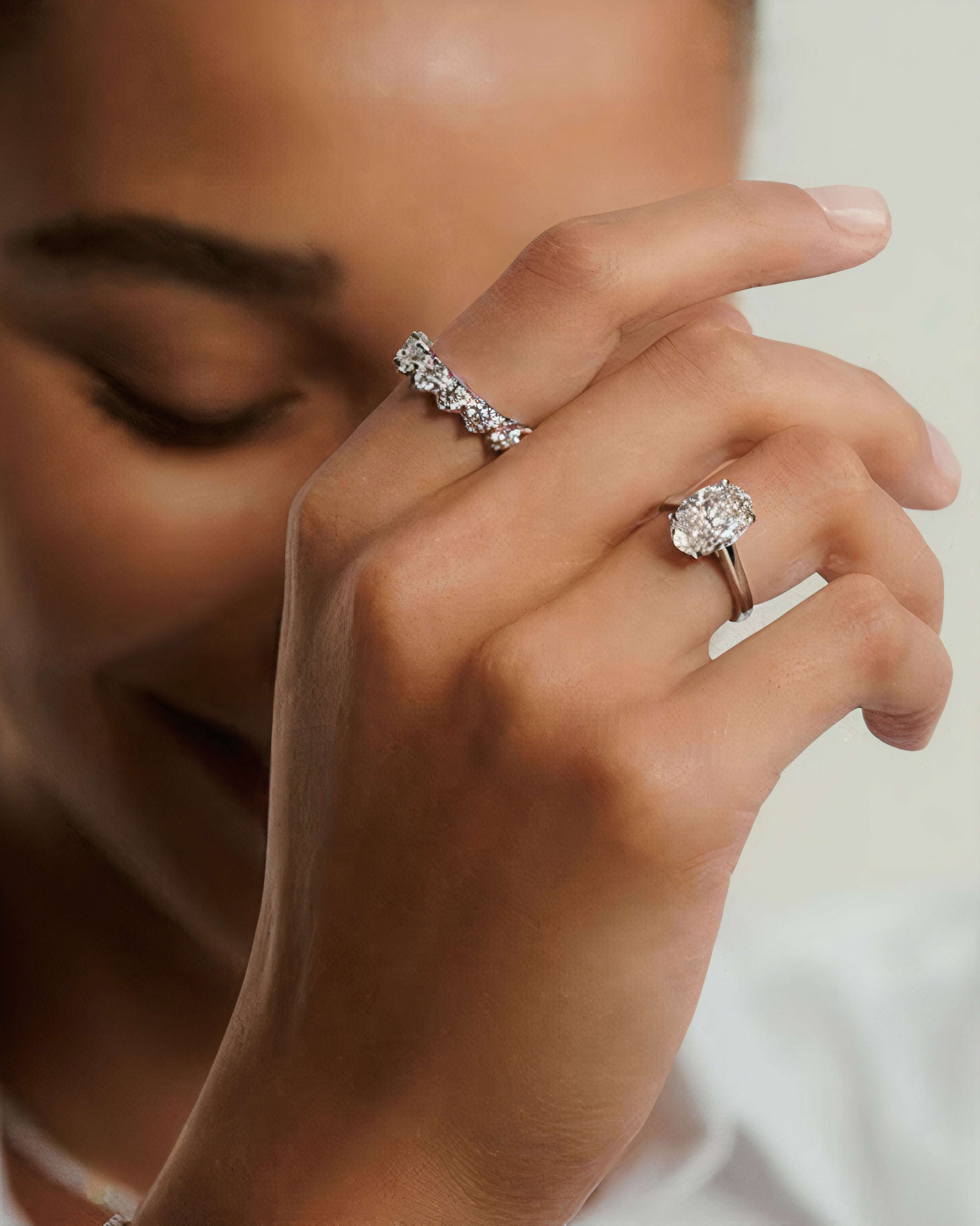 Close-up of smiling model’s hand wearing three eternity bands and a round cut solitaire ring.