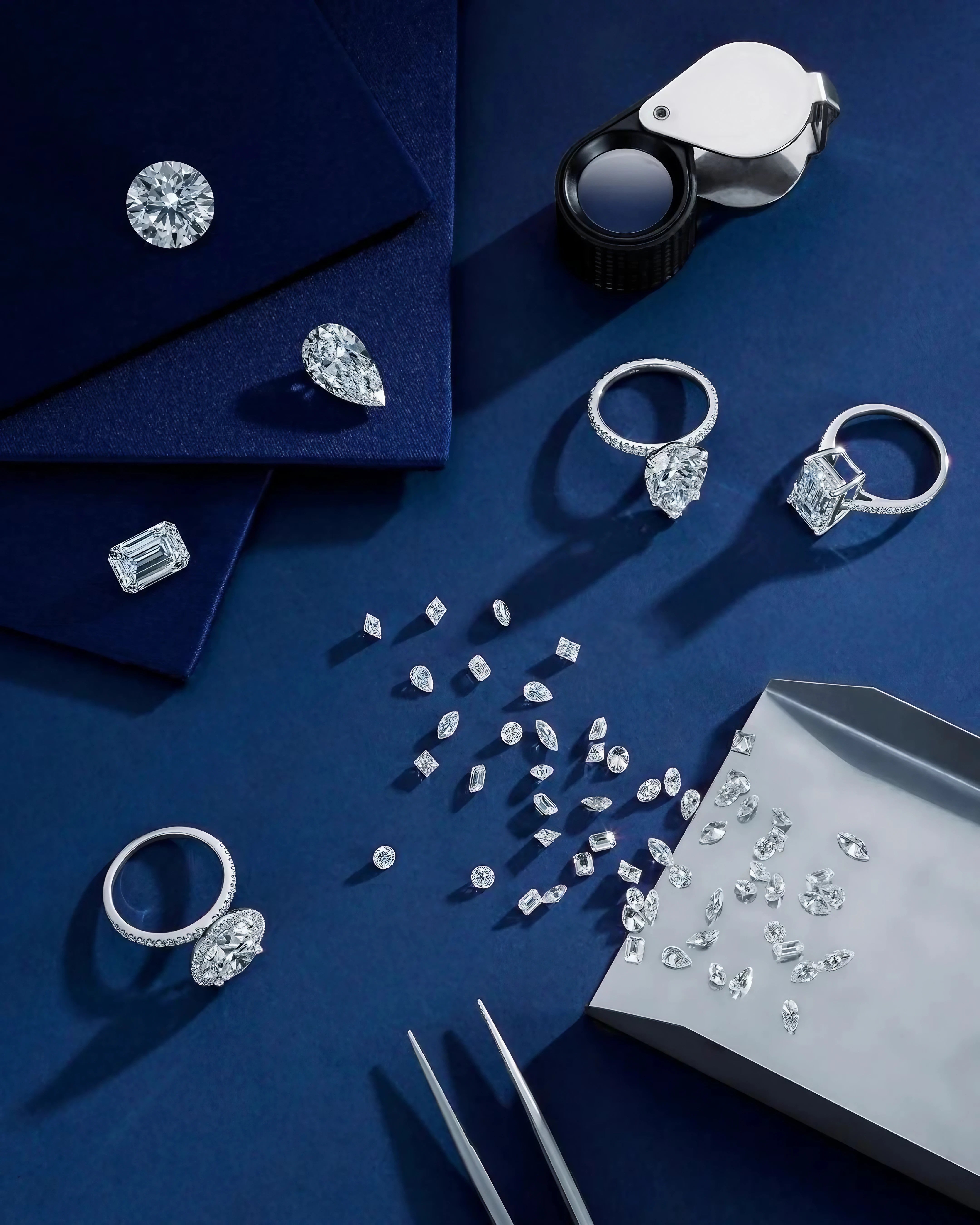 Assortment of loose diamonds and finished rings styled elegantly on a sapphire blue cloth.