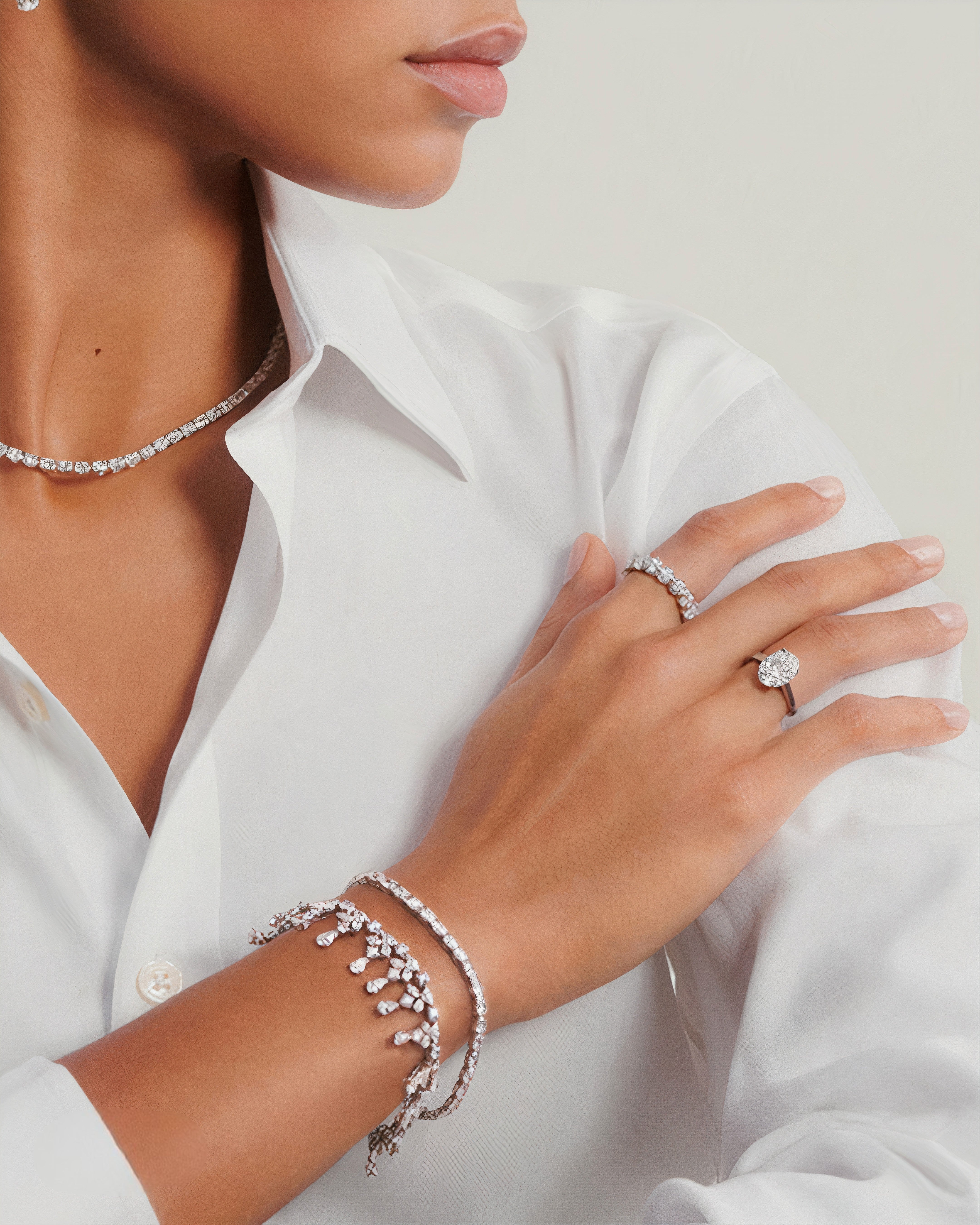 Model crossing arms, wearing a tennis necklace and round cut engagement ring with eternity bands.