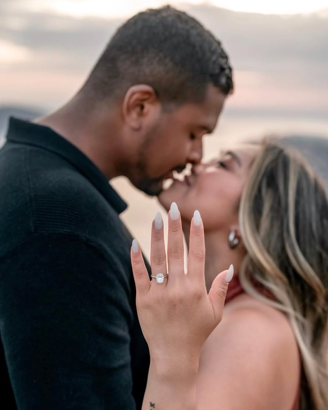 Couple kisses after proposal, while the bride-to-be lifts her hand showing off the engagement ring.