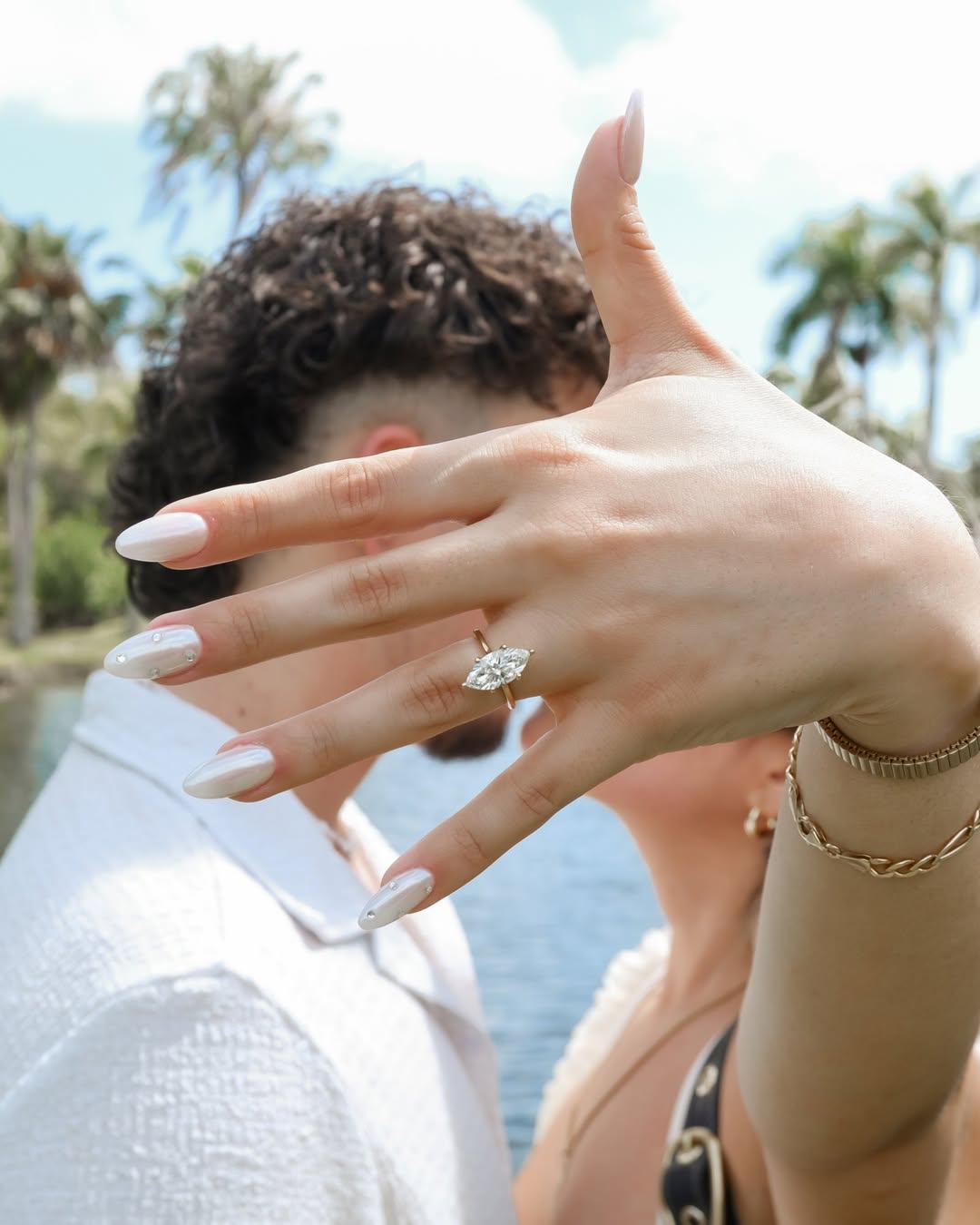 Hand raised toward sunlight with palm trees in the background, showcasing a sparkling ring moment.