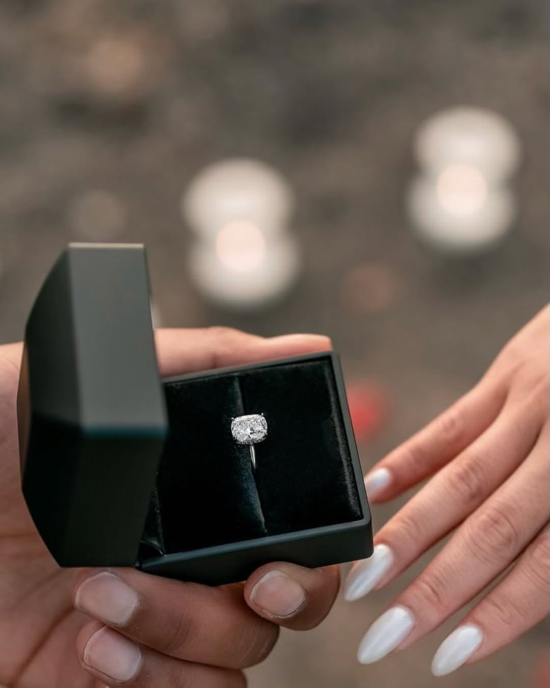 Engagement ring in a black box being handed over during a romantic outdoor proposal scene.
