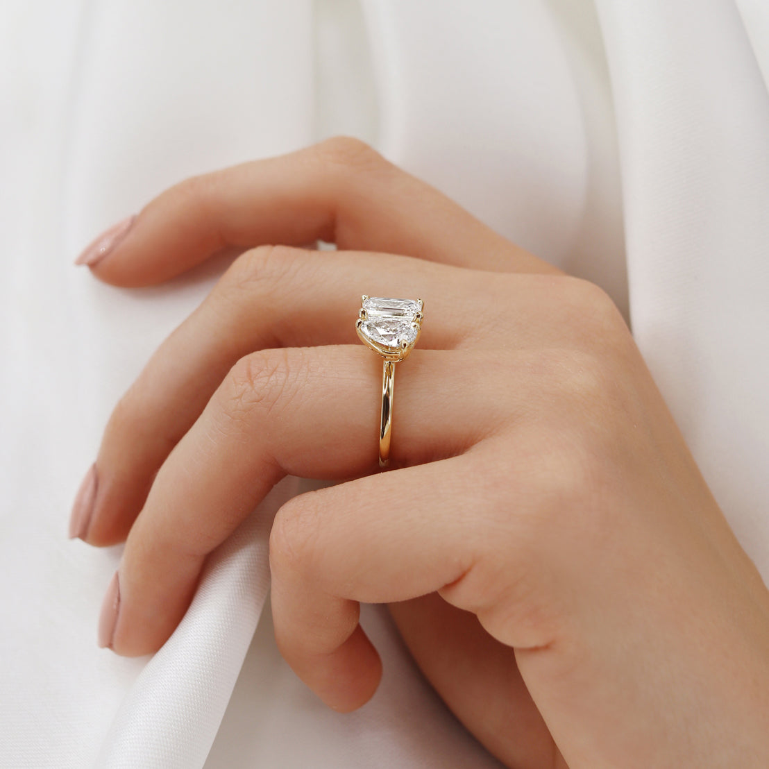 Side hand view of emerald and pear cut lab diamond Toi Et Moi ring in 18k yellow gold