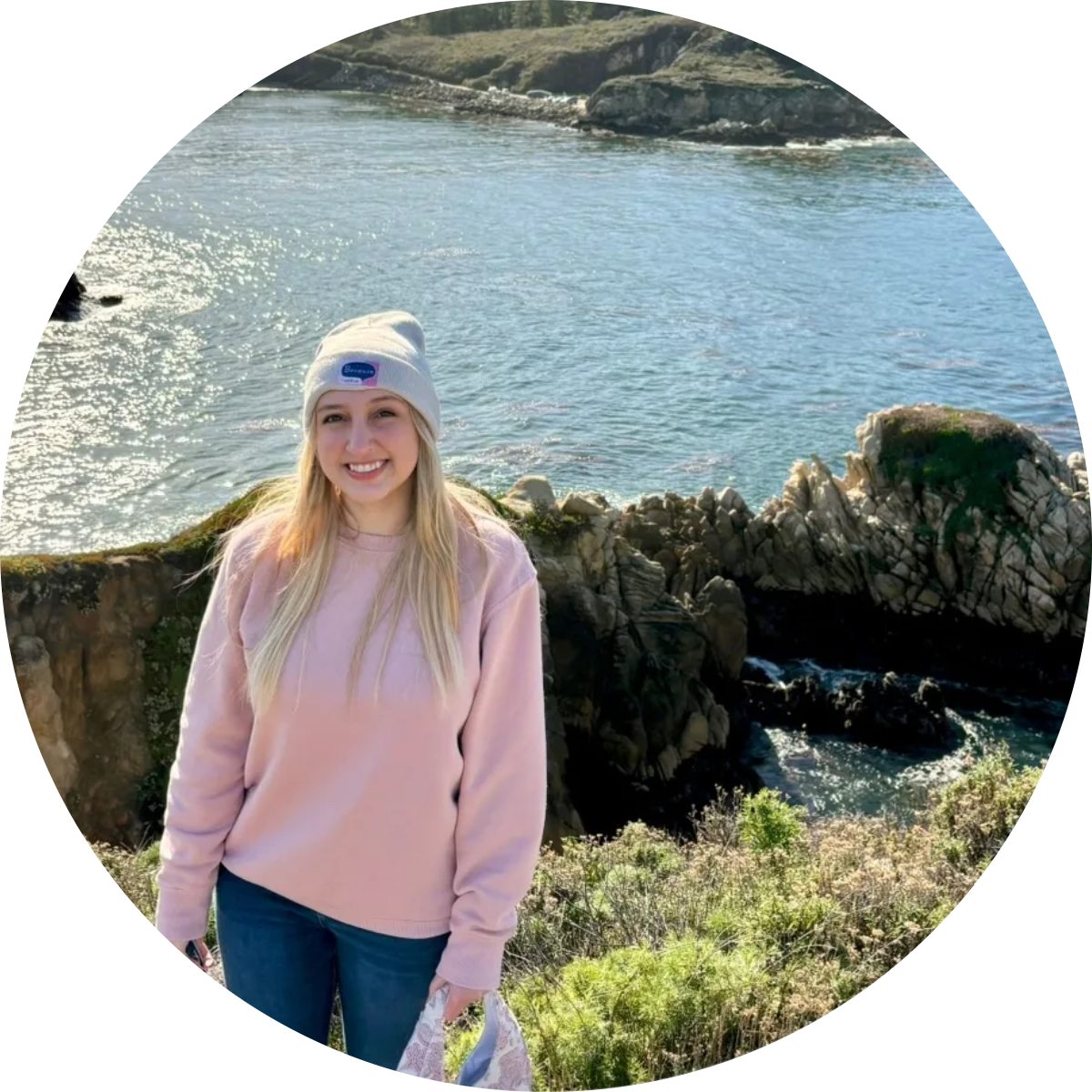 Woman in pink sweater and beanie standing by the seaside cliffs with ocean background