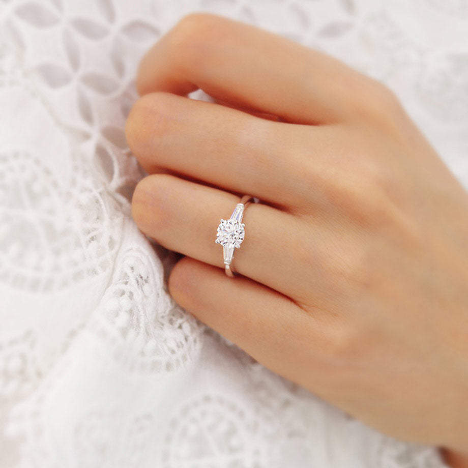 Model wearing AZALEA 18k yellow gold trilogy engagement ring with round centre diamond and baguette side stones, elegant close-up