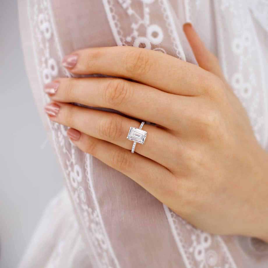 Model wearing solitaire emerald cut lab diamond ring in 18k white gold pavé band