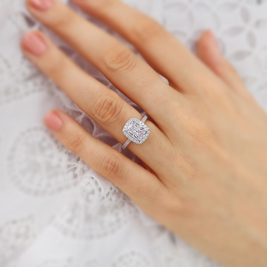 Woman wearing elongated cushion cut lab diamond halo engagement ring in 18k rose gold, close-up hand view