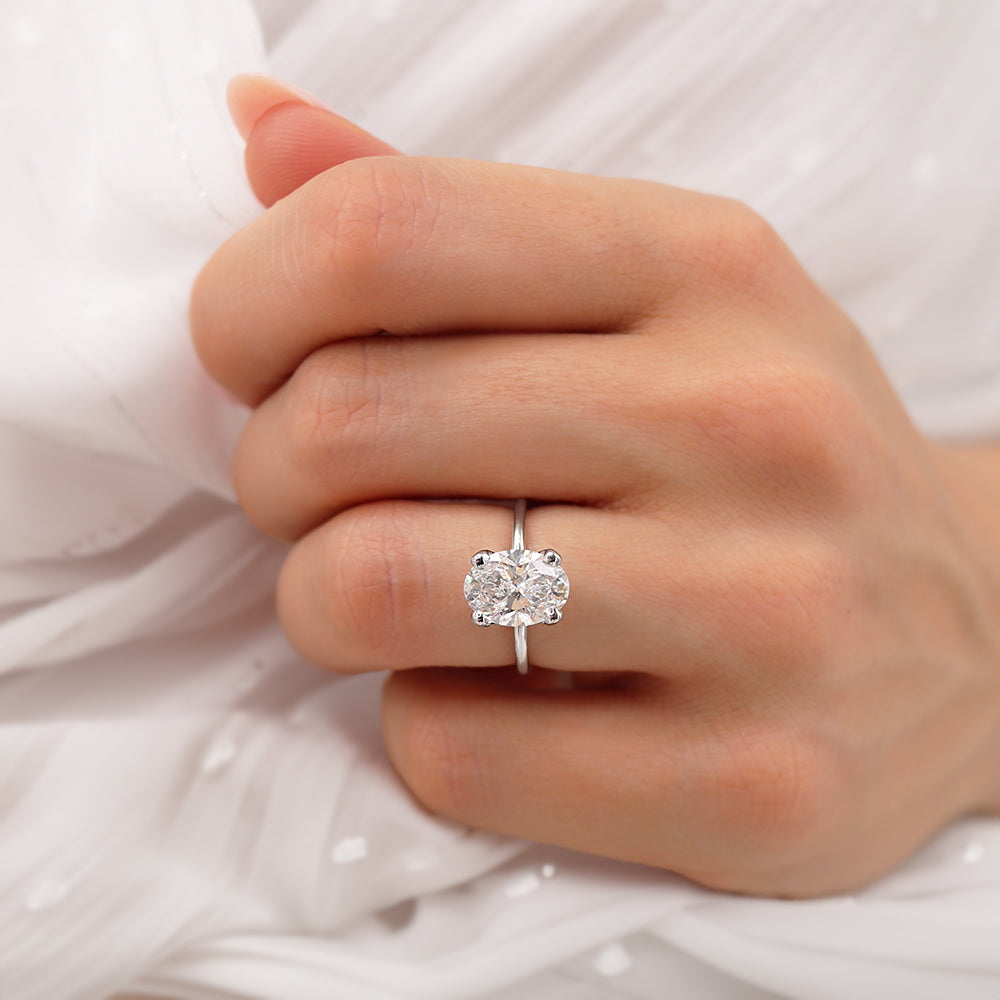 Close-up of 18k white gold oval lab diamond ring on hand, wrapped in soft fabric