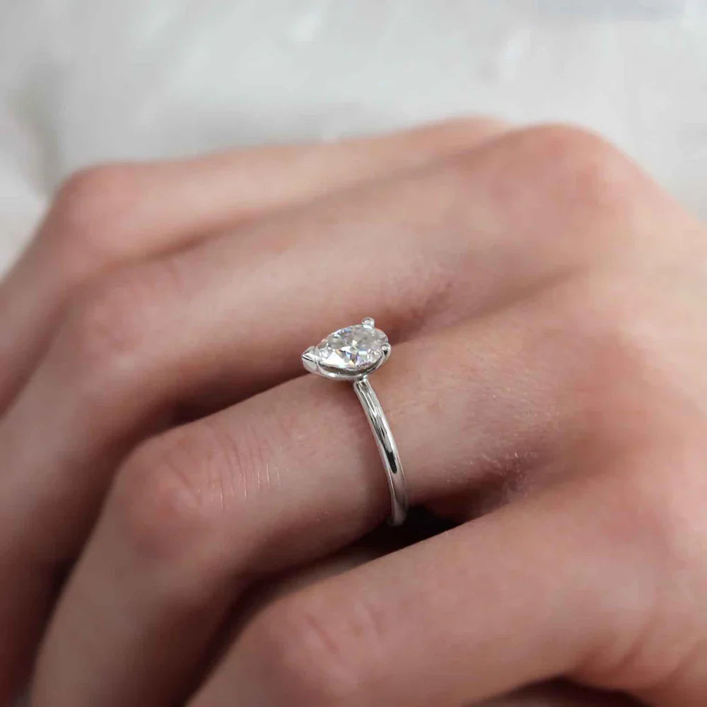 Woman wearing pear cut lab diamond solitaire engagement ring in platinum, close-up hand view