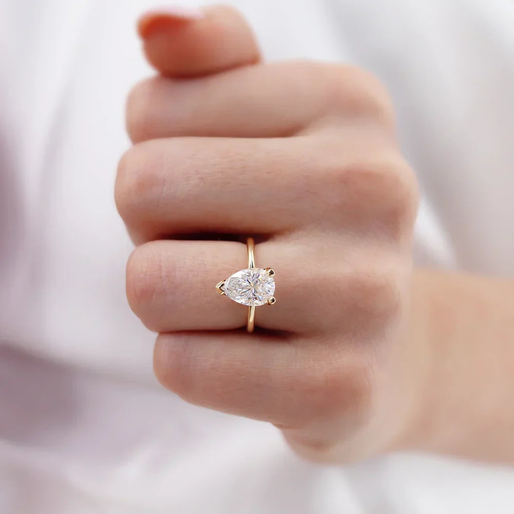 Woman wearing pear cut lab diamond solitaire engagement ring in 18k yellow gold, close-up hand view