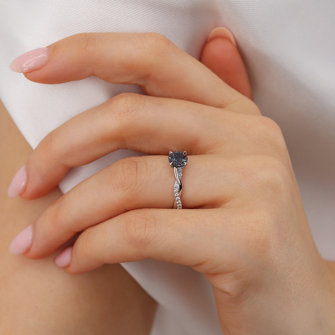 Close-up hand pose highlighting the sculptural vine motif and the vivid brilliance of the center stone in soft daylight.